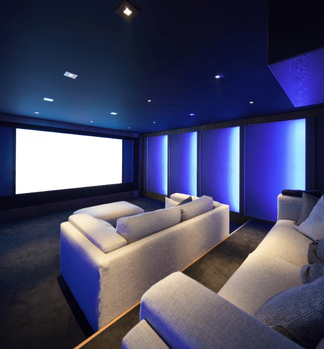 Basement home theater with projection screen, blue accent lighting, and plush sofas
