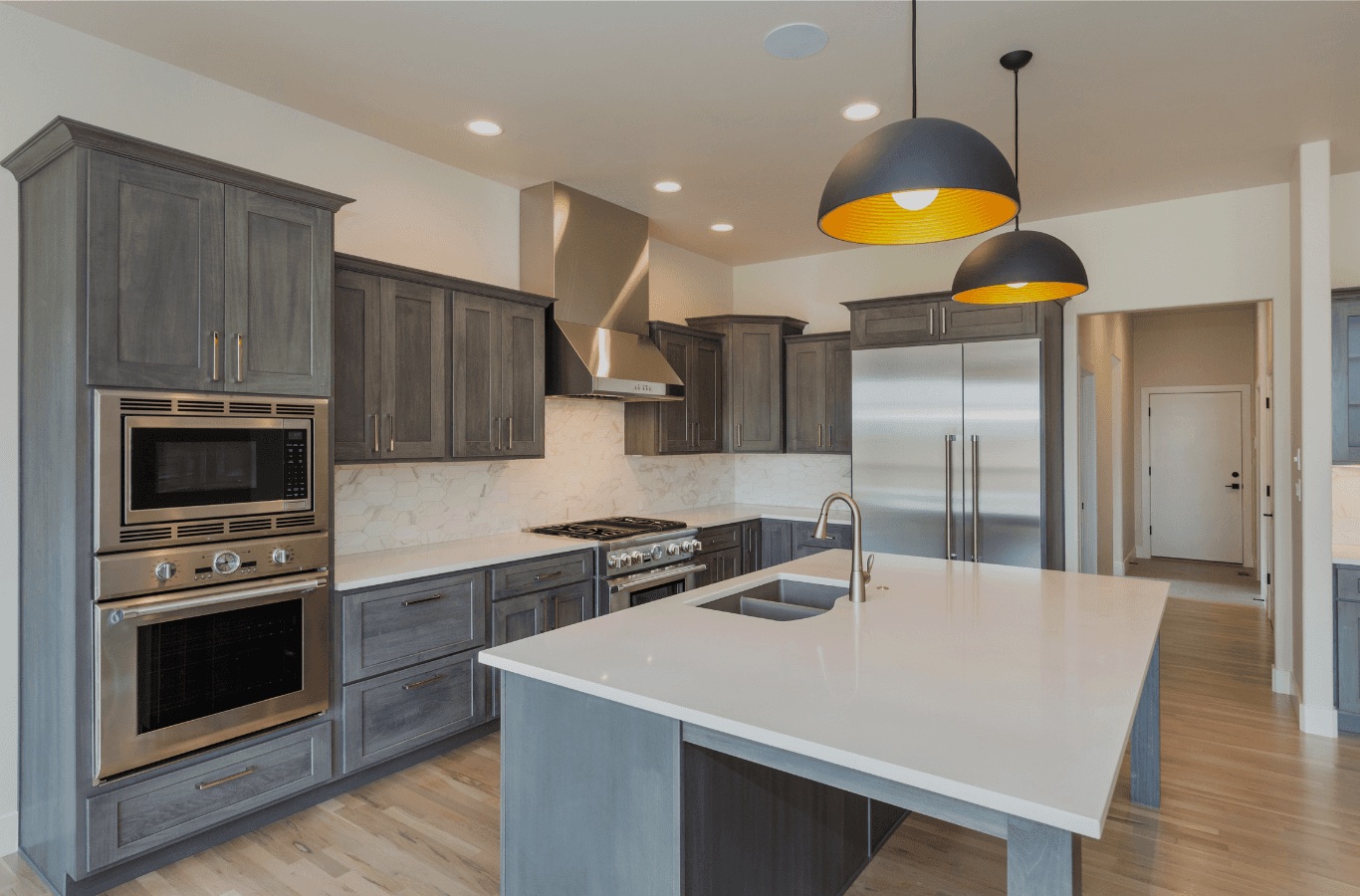 Remodeled kitchen with gray custom cabinetry, a large white island, and warm pendant lighting