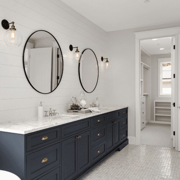 Remodeled bathroom with navy double vanity, marble counters, and round mirrors